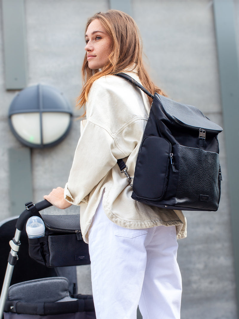 Storksak Alyssa | convertible Changing bag Backpack | Leather Baby Bag | mum wearing Black diaper Bag as backpack and pushing pram